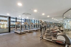A gym with multiple treadmills and elliptical machines, large windows, and a modern interior design. - Luxe 2BR Retreat POOL, GYM & PARKING South Yarra (South Yarra)
