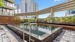 Ein Pool auf dem Dach mit Glasabdeckung, umgeben von Steinfliesen und einer Holzterrasse.