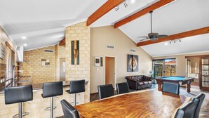 A spacious room with a large wooden dining table surrounded by chairs, a pool table, and a bar area with stools. - Spacious 5-bedroom house with pool and park access  in serene Ocean Reef with AC (Ocean Reef)