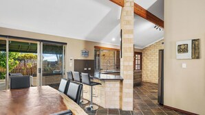 A modern kitchen with a stone column, a dining area with a wooden table and black chairs, and a view of the outdoors through large sliding glass doors. - Spacious 5-bedroom house with pool and park access  in serene Ocean Reef with AC (Ocean Reef)