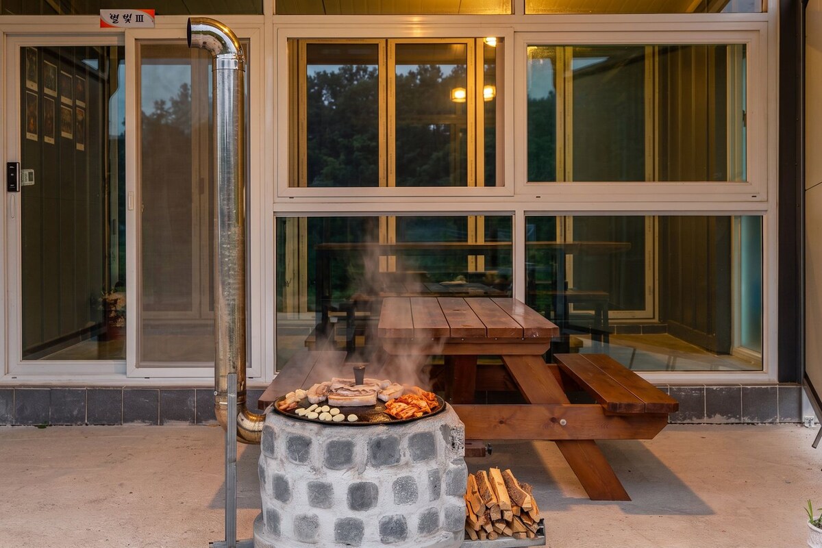 Ein Grill mit Essen im Freien, ein Holztisch und eine Glastür, die zu einer Terrasse führt.