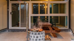 Een buitenbarbecue met eten, een houten tafel en een glazen deur die uitkomt op een terras.