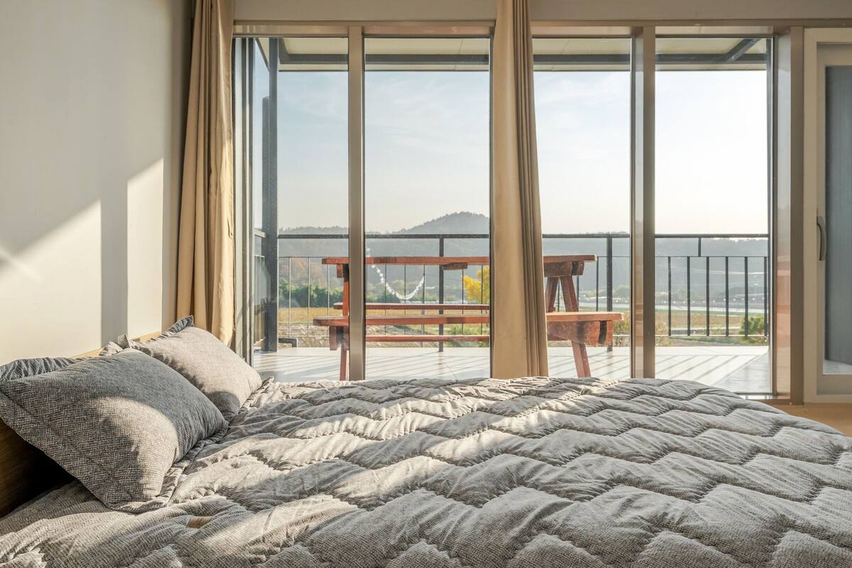 Een slaapkamer met een groot bed, een houten hoofdbord en uitzicht op een balkon met een tafel en stoelen.