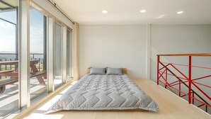 Un dormitorio con un ventanal grande, una cama con colcha y una barandilla roja.