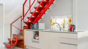 Een moderne keuken met een rode trap, een magnetron, een waterkoker en een spoelbak.