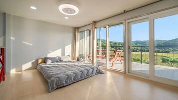 A bedroom with a large bed, a wooden floor, and a balcony with a view of the countryside.
