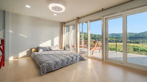 Ein Schlafzimmer mit einem großen Bett, Holzboden und einem Balkon mit Blick auf die Landschaft.