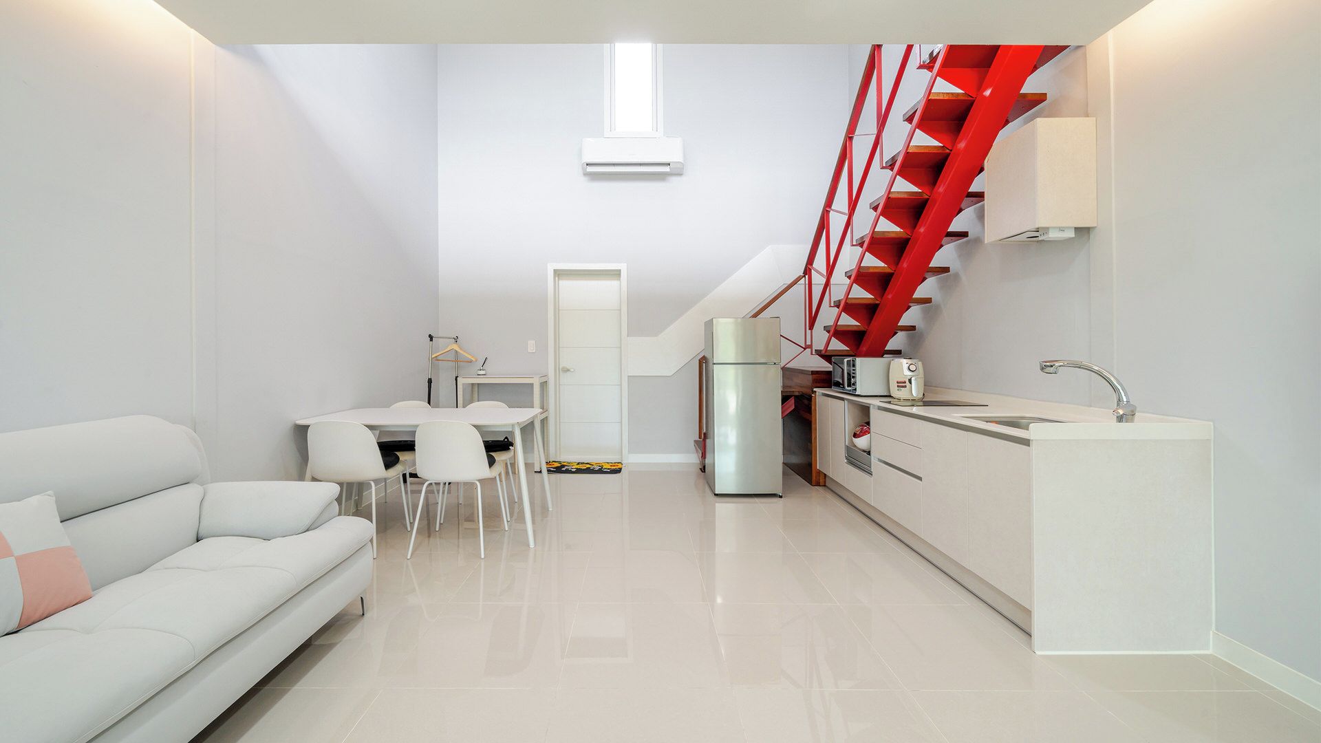 A compact living space with a kitchenette, a dining area, and a staircase with red railings.