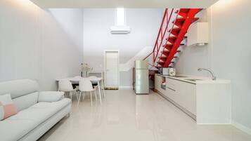 A compact living space with a kitchenette, a dining area, and a staircase with red railings.