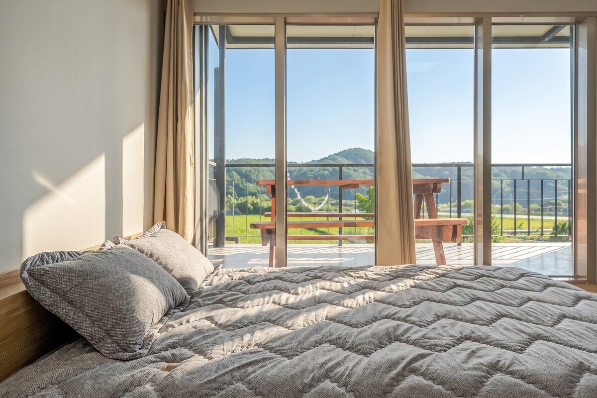 Ein Schlafzimmer mit einem großen Bett, Blick auf einen Balkon mit einem Holztisch und einer reizvollen Landschaft.