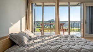 A bedroom with a large bed, a view of a balcony with a wooden table, and a scenic landscape. - Gyeongju Starlight Pension (Gyeongju)