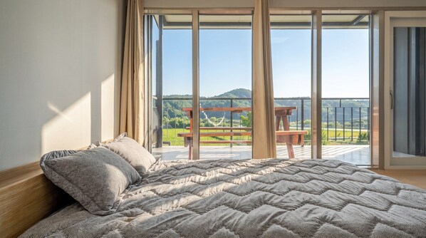 Quarto com uma cama grande, vista para uma varanda com mesa de madeira e paisagem panorâmica.