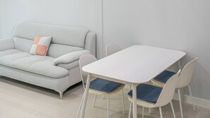 Een moderne woonkamer met een grijze bank, een witte tafel en bijpassende stoelen.