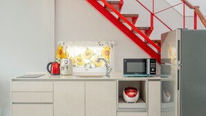 Een moderne keuken met een magnetron, waterkoker en koffiezetapparaat op het aanrecht, een spoelbak en een rode trap op de achtergrond.