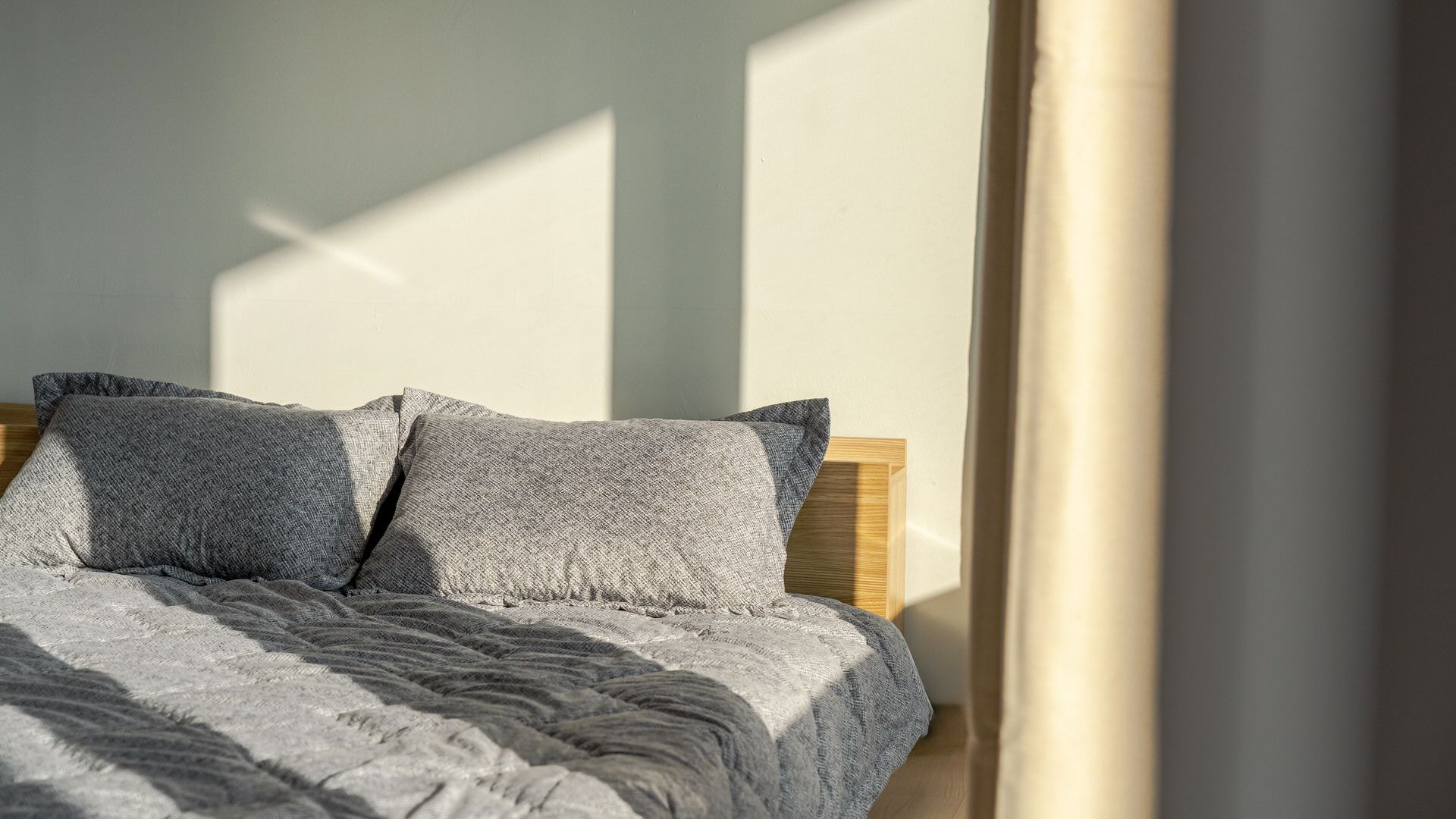 Una cama con cabecera de madera y ropa de cama gris.
