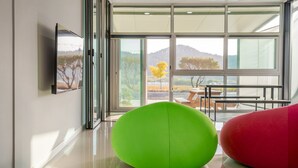 Un interior moderno con un ventanal grande, una silla verde y una silla roja, y un cuadro enmarcado en la pared.