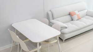 Une pièce moderne et minimaliste, avec une table blanche et des chaises assorties, un canapé gris agrémenté d’un seul coussin, et un mur blanc uni.