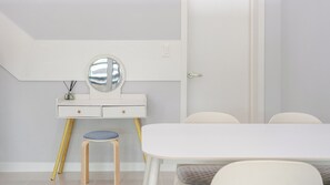 Ein stilvolles, minimalistisches Zimmer mit einem weißen Schminktisch, einem runden Spiegel, einem Hocker und einem Esstisch mit Stühlen.