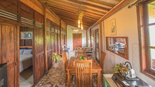 A wooden interior with a dining table, chairs, a kitchen area, and a bed. - Breeze and Blossom Cottage Maguwo (Depok)