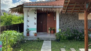 A house with a tiled roof, a wooden door, and a small porch with potted plants. - Breeze and Blossom Cottage Maguwo (Depok)