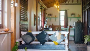 A cozy room with a wooden bench, a plant, and a dining area in the background. - Breeze and Blossom Cottage Maguwo (Depok)