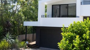 Una casa moderna de dos pisos con garaje, rodeada de exuberante follaje y árboles.