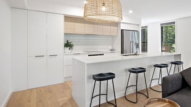 Una cocina moderna con armarios blancos, una isla central con taburetes y una lámpara colgante.