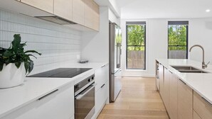 Una cocina moderna con armarios blancos, horno empotrado y un amplio ventanal con vistas a zonas verdes.