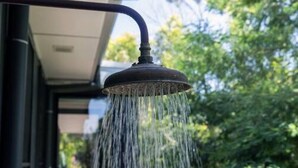 Un cabezal de ducha con agua saliendo, adosado al exterior de un edificio.