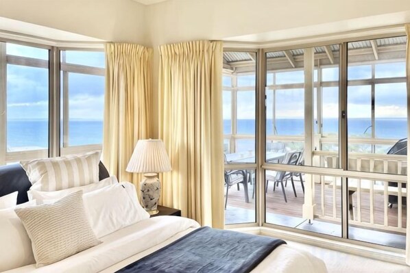 A hotel room with a large bed, a nightstand, a lamp, and a view of the ocean through large windows. - Ocean View Holiday Home Near Beach in Mount Martha (Mount Martha)