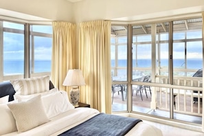 A hotel room with a large bed, a nightstand, a lamp, and a view of the ocean through large windows. - Ocean View Holiday Home Near Beach in Mount Martha (Mount Martha)
