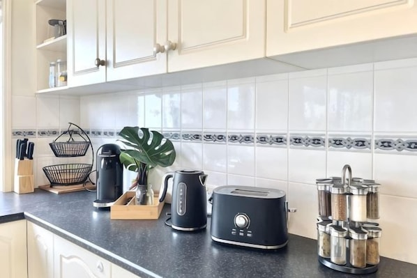 A kitchen with white cabinets, a black countertop, and a backsplash with a decorative pattern. - Ocean View Holiday Home Near Beach in Mount Martha (Mount Martha)