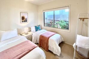 A bedroom with two beds, a bedside table with a lamp, a window with a view, and a crib. - Ocean View Holiday Home Near Beach in Mount Martha (Mount Martha)