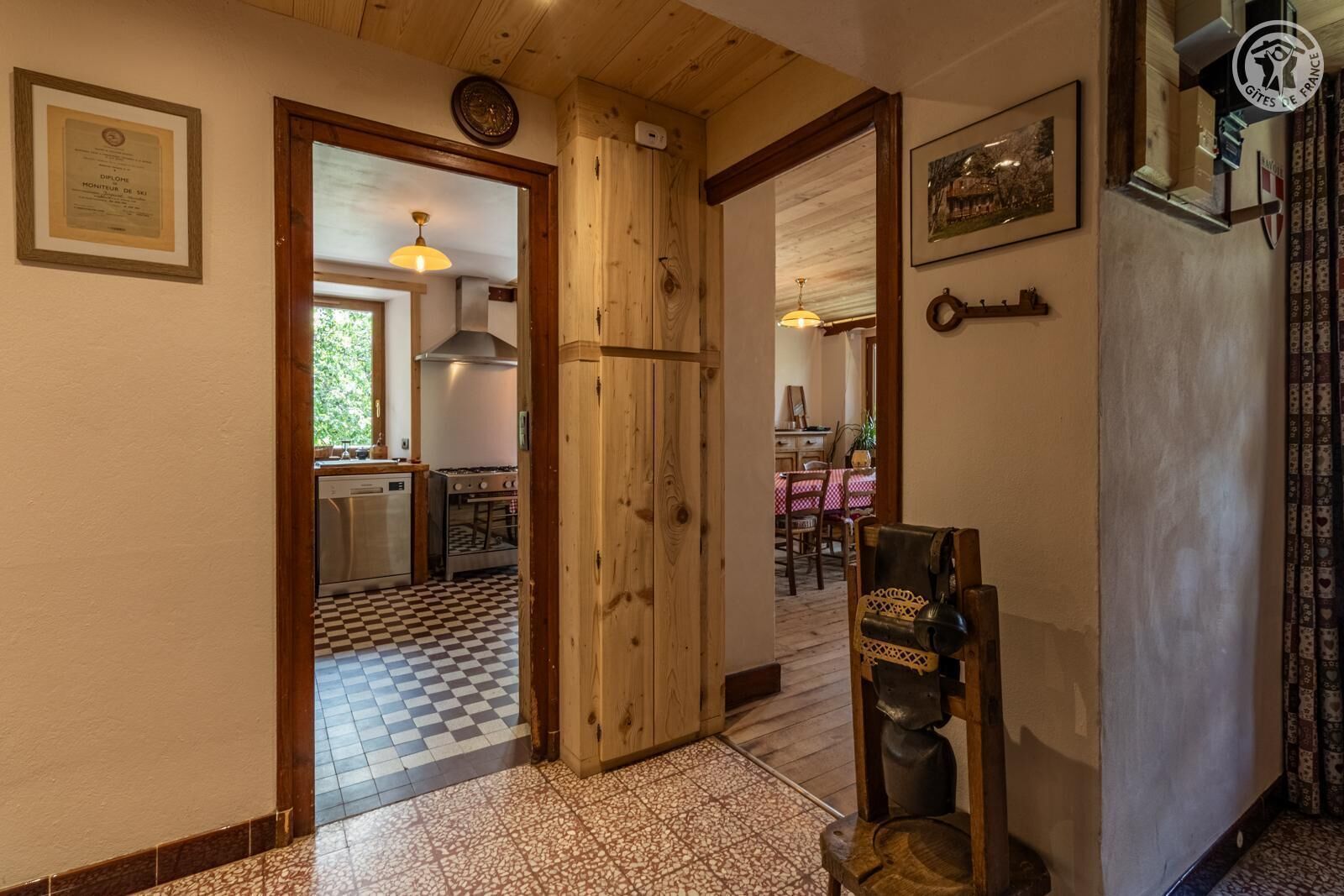 Un pasillo con piso de cuadros que conduce a una zona de cocina, una puerta de madera y un comedor con mesa y sillas.
