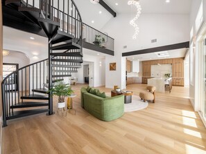 Ein großzügiger Wohnbereich mit einer schwarzen Wendeltreppe, einem grünen Sofa und einer Küche im Hintergrund.