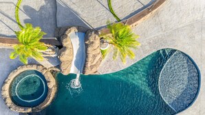 Vista aérea de una piscina con cascada, rodeada de rocas y palmeras.