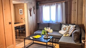 Una sala de estar acogedora con un sofá gris, una mesa de centro negra y una mesa de comedor de madera.