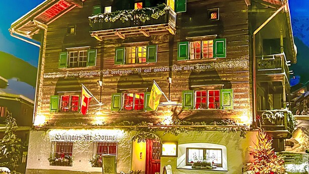 Un edificio de madera tradicional con varias ventanas, algunas con contraventanas verdes, y un letrero sobre la entrada.