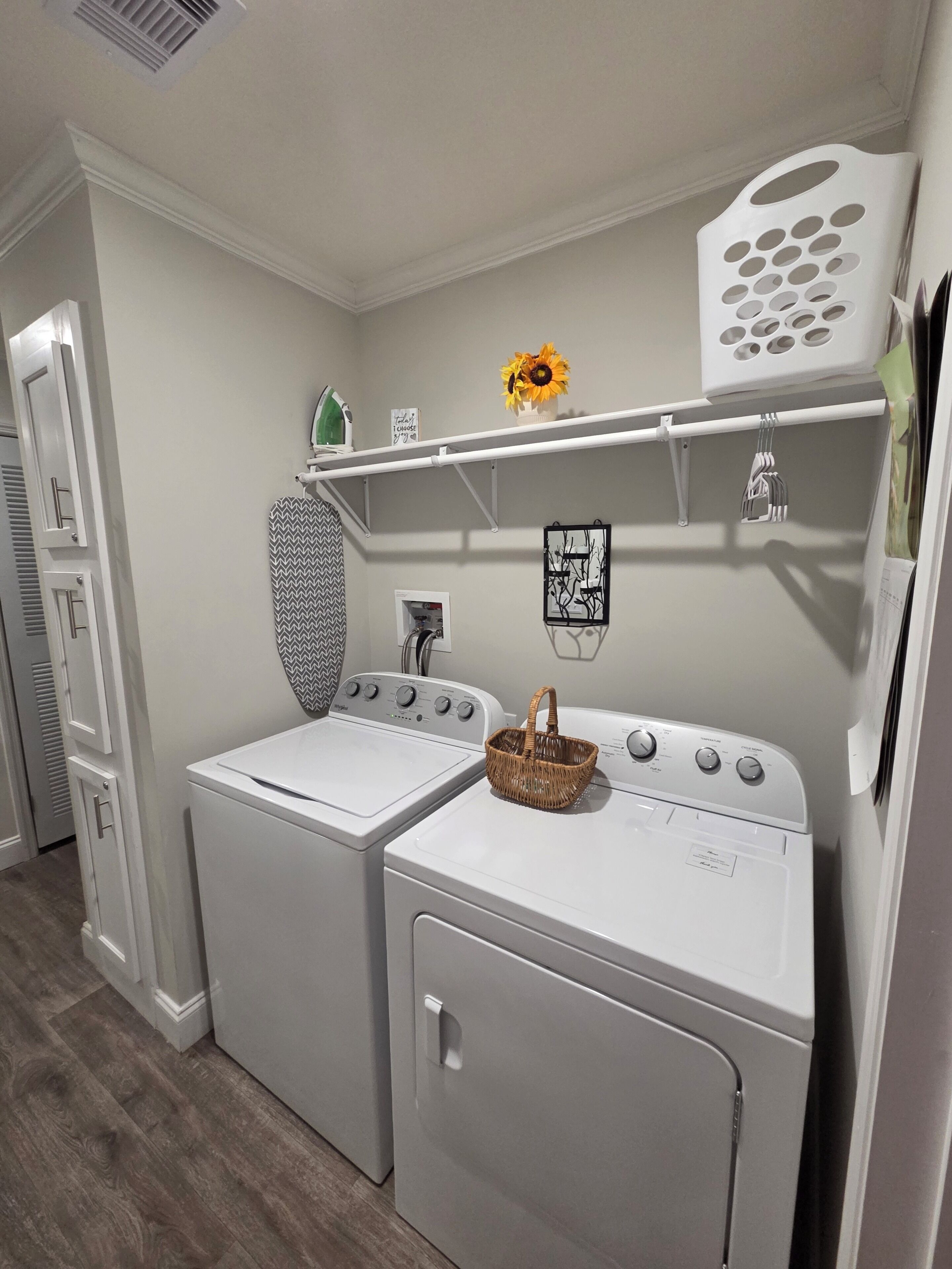 A laundry room with two stacked washing machines, a drying rack, a shelf with a basket, and a wall-mounted drying rack.
