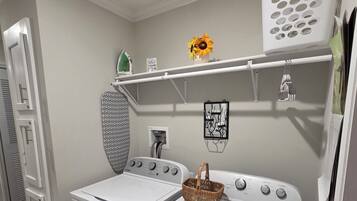 A laundry room with two stacked washing machines, a drying rack, a shelf with a basket, and a wall-mounted drying rack.