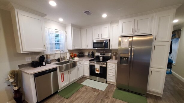 A modern kitchen with white cabinets, stainless steel appliances, and a green rug.