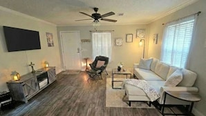 A living room with a ceiling fan, a sofa, a chair, a coffee table, and a TV mounted on the wall.