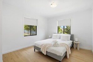 Un dormitorio con cama, mesita de noche, espejo y ventana.