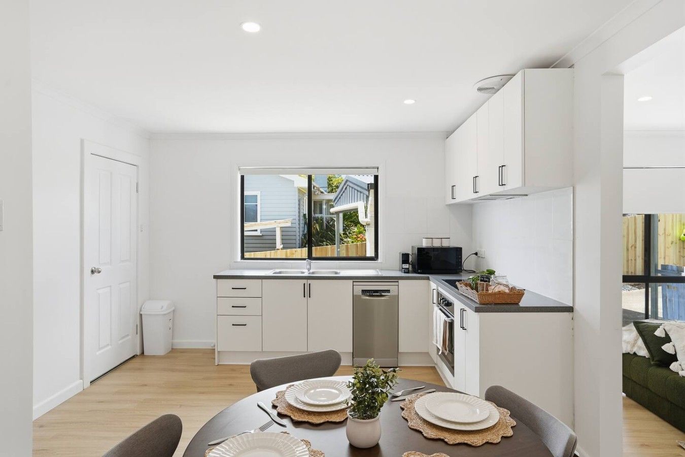 Cocina moderna con armarios blancos, lavavajillas integrado y ventana con vistas a un jardín.