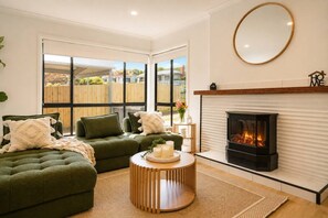 Una sala de estar con chimenea, sofás verdes y un ventanal grande.
