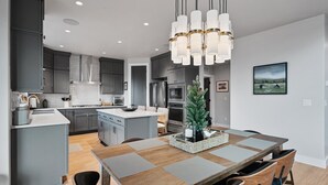 A modern kitchen with grey cabinets, a central island, and a dining area with a wooden table and chairs. - Deer Valley Views, 5br Sleeps 16, Hot Tub, Theater (Heber City)