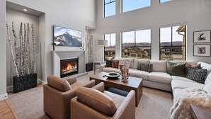 A spacious living room with a fireplace, large windows, and a view of a mountain. - Deer Valley Views, 5br Sleeps 16, Hot Tub, Theater (Heber City)