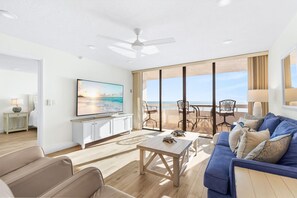 Een moderne woonkamer met een flatscreen televisie, een houten salontafel, een blauwe bank en een balkon met uitzicht op zee.