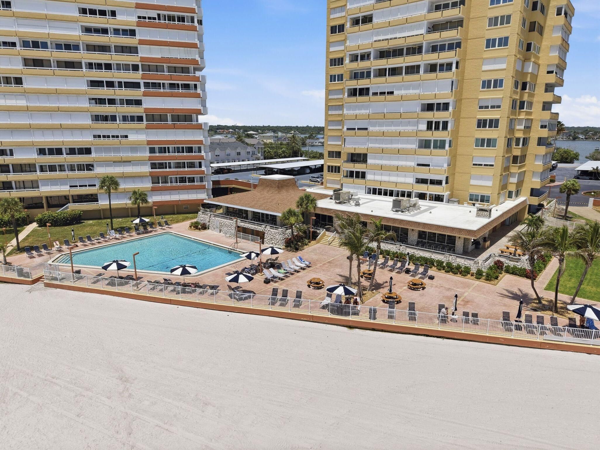 A high-rise hotel with a rooftop pool, multiple balconies, and a landscaped pool area with sun loungers and umbrellas.