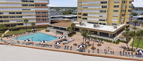 A high-rise hotel with a rooftop pool, multiple balconies, and a landscaped pool area with sun loungers and umbrellas.